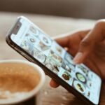 Hand browsing social media photos on a smartphone next to a cup of coffee indoors.